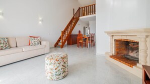 Una sala de estar con sofá, reposapiés, chimenea, mesa de comedor, sillas y una escalera.