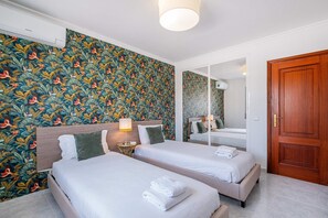 Quarto de hotel com duas camas, um espelho, uma porta de madeira e parede com padrão floral.