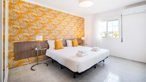 Una habitación de hotel con una cama grande, un cabecero, una mesita de noche con lámpara y una ventana con cortinas.
