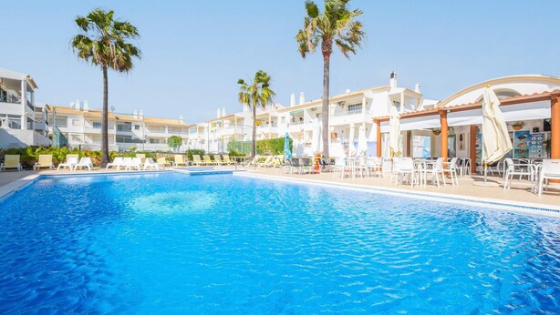 Una piscina con sillas de descanso y palmeras, rodeada de edificios de varios pisos.