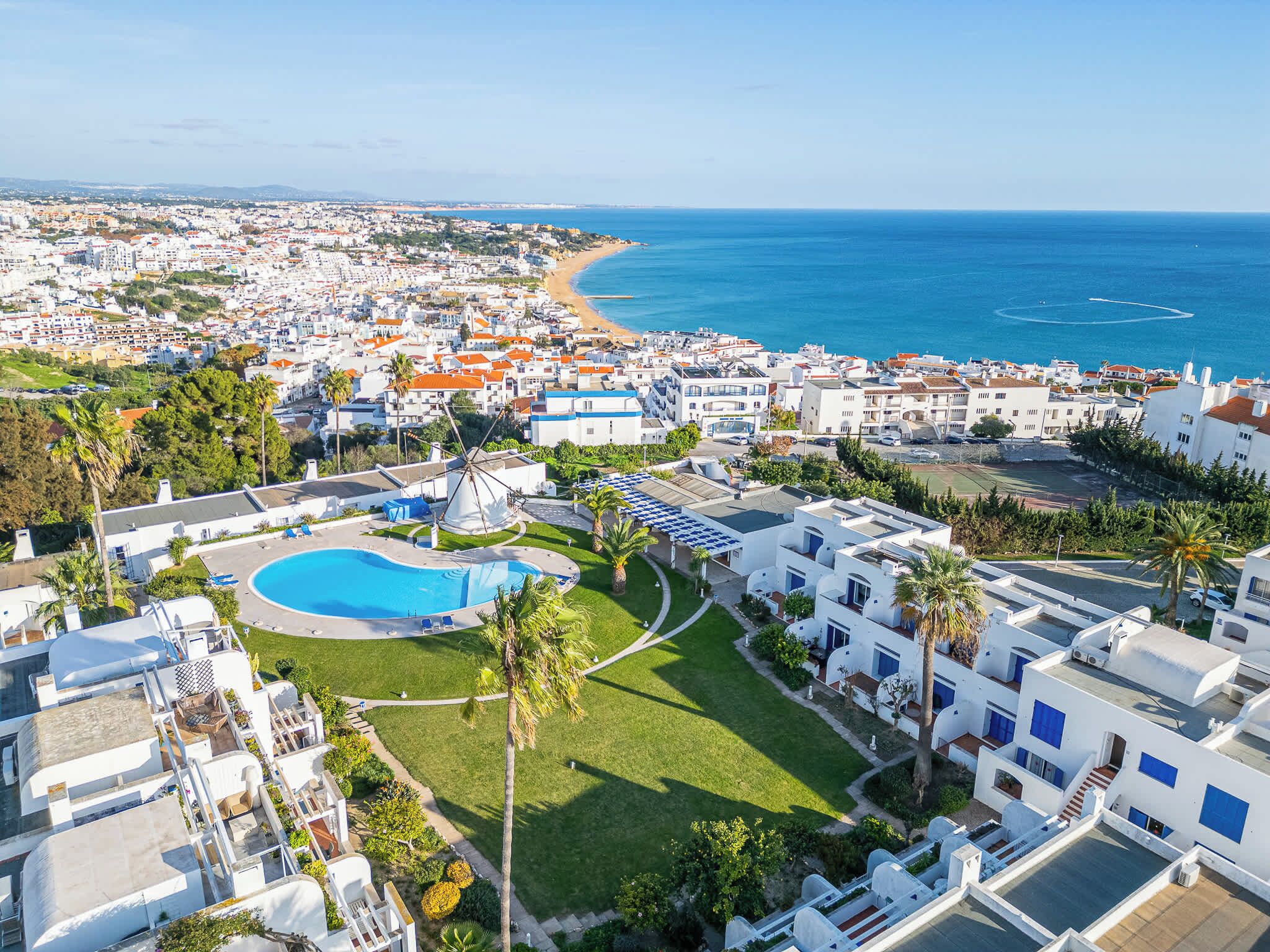 Un resort costero con piscina, palmeras y vistas al mar.