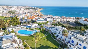 A coastal resort with a swimming pool, palm trees, and a view of the sea. - Apartment Vento - Complex great for families (Albufeira)