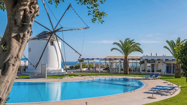 A swimming pool with a windmill, palm trees, and a building with a blue and white facade. - Apartment Vento - Complex great for families (Albufeira)