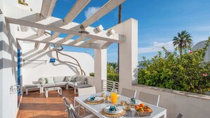An outdoor patio with a white table set for breakfast, a sofa, and a pergola structure. - Apartment Vento - Complex great for families (Albufeira)