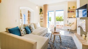A modern living room with a beige sofa, a small round table, and a TV. There is a sliding glass door leading to an outdoor area with a table and chairs. - Apartment Vento - Complex great for families (Albufeira)
