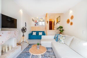 A modern living room with a TV, a blue sofa, a white sofa, a coffee table, and a staircase leading to a kitchen. - Apartment Vento - Complex great for families (Albufeira)