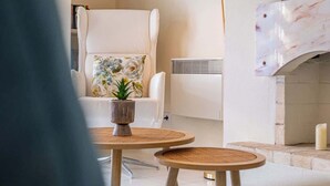 A living room with a white armchair, a small round table with a plant, a floor lamp, a flat-screen TV, and a fireplace. - Apartment Vento - Complex great for families (Albufeira)