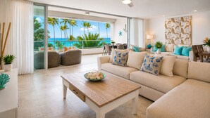 Un vaste salon doté d’une grande fenêtre donnant sur une plage, d’un ventilateur de plafond et d’un coin repas avec vue.