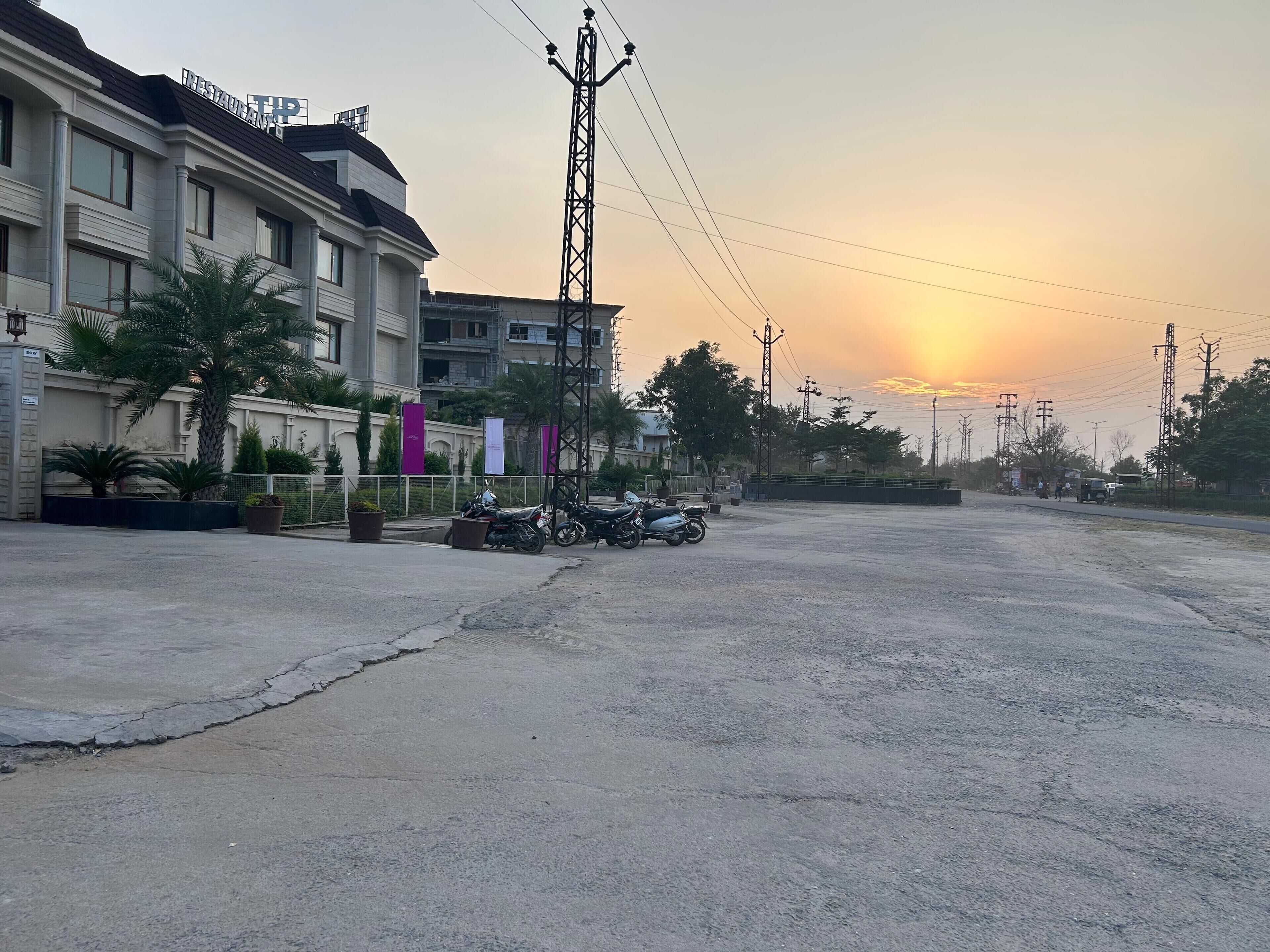 A parking area with motorcycles, a building with columns, and a sunset in the background.