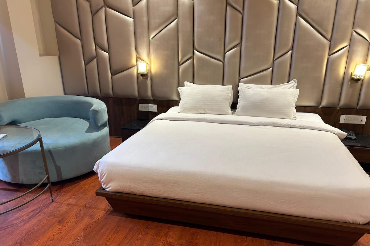 A modern hotel room with a large bed, a side table, a chair, and a wall-mounted light fixture.
