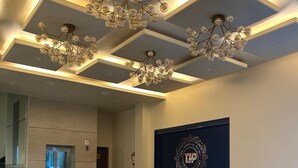 Um hall espaçoso com um lustre moderno, um grande brasão emoldurado na parede e uma escadaria que dá acesso a um elevador.