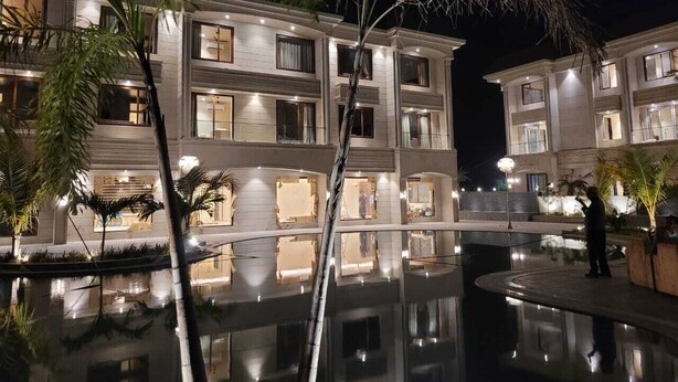 Um hotel com vários andares, piscina refletora, palmeiras e varandas bem iluminadas.