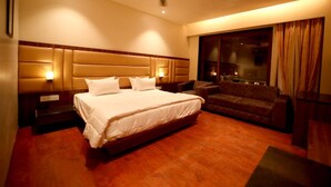 Quarto de hotel com uma cama grande, um sofá, uma televisão e uma janela com cortinas.