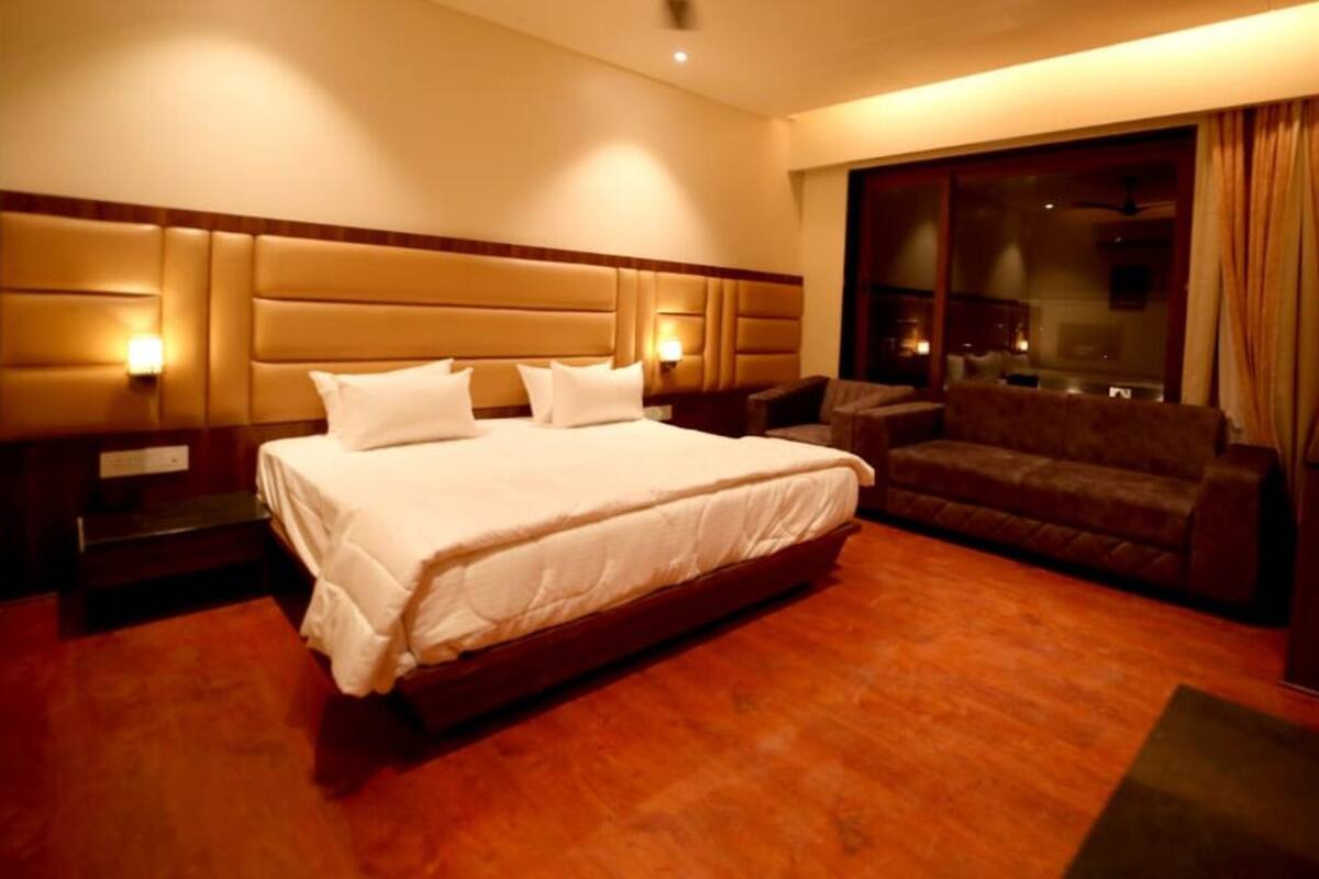 A hotel room with a large bed, a sofa, a TV, and a window with curtains.