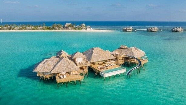 Bungalows op het water met rieten daken, een zwembad en helder uitzicht op de oceaan.