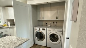 A compact kitchen with white cabinets, a granite countertop, and a built-in washer and dryer. - Beautifully updated home in the South Hills (Missoula)