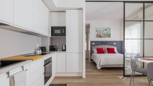 A modern hotel room with a kitchenette, a bed with red pillows, and a large window. - Delightful apartment in Ponte Milvio district (Roma)