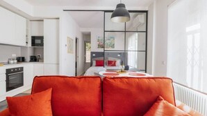 A modern kitchen with white cabinets, a black oven, and a dining area with a red sofa and a table. - Delightful apartment in Ponte Milvio district (Roma)