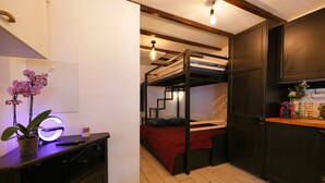 Een compacte kamer met een stapelbed, een bureau met lamp en een kleine plant.