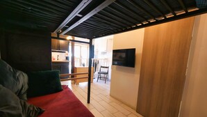 Een slaapkamer met een bed, een rode deken, een houten garderobe en een aan de muur bevestigde televisie.