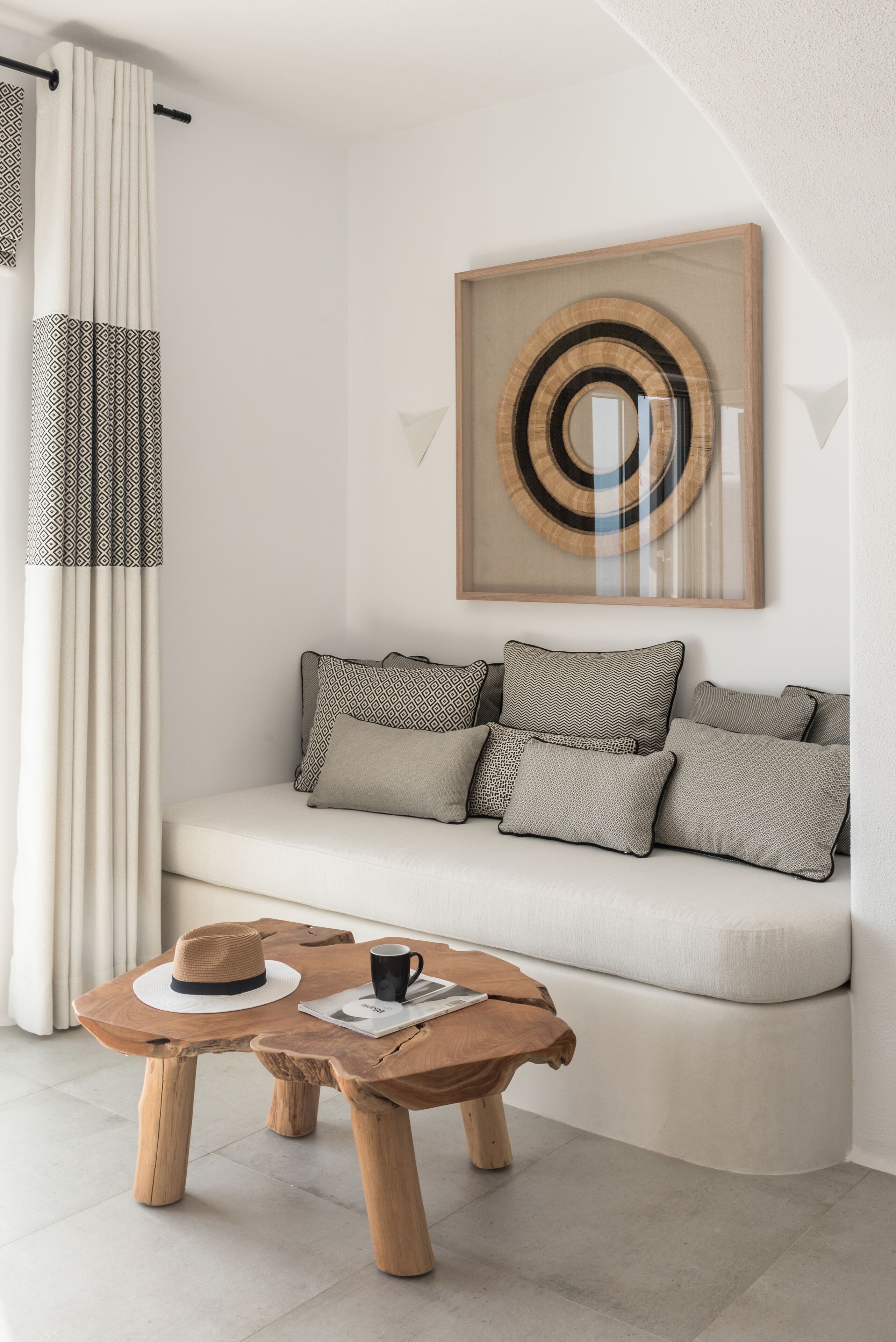 Un salon moderne avec un canapé, des coussins à motifs, une table basse en bois, un chapeau, une tasse et une œuvre d’art encadrée accrochée au mur.