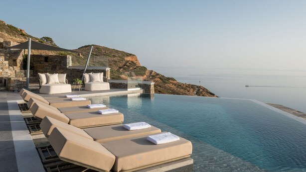 Una piscina infinita con sillones de descanso y una estructura de piedra al fondo.
