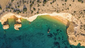 Vista aérea de una zona costera con aguas turquesas cristalinas, formaciones rocosas y vegetación escasa.