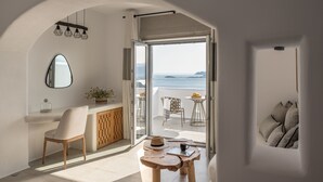 Habitación moderna y minimalista con vista al mar, un escritorio de madera, una silla y una mesita con un sombrero y una taza.
