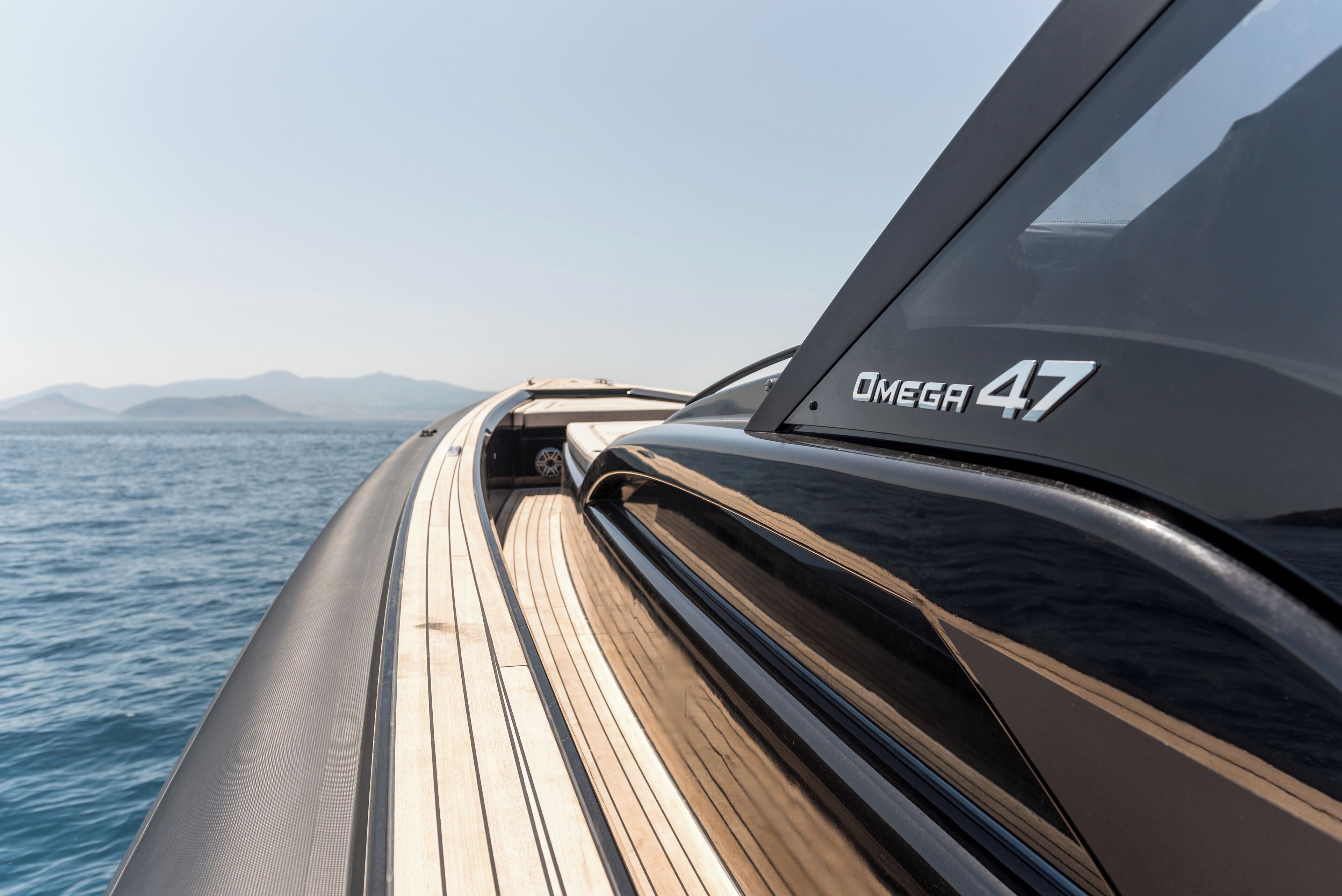 The side of a boat with the text "OMEGA 47" and a view of the sea and mountains in the background.