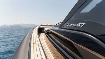 The side of a boat with the text "OMEGA 47" and a view of the sea and mountains in the background.