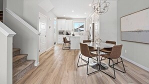Una cocina moderna con armarios blancos, un comedor con una mesa redonda y sillas, y una escalera que sube a otro nivel.