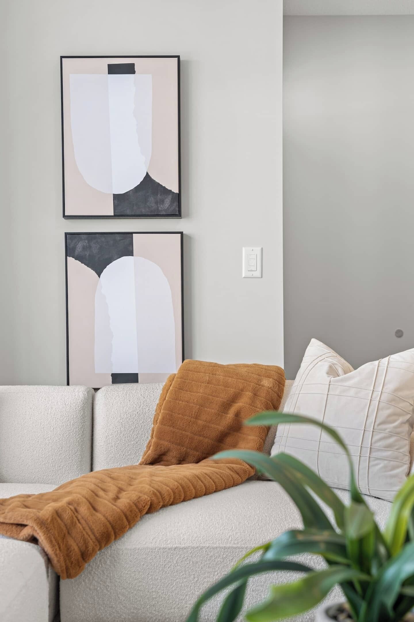 A modern living room with a sofa, a brown throw blanket, and two abstract wall art pieces.