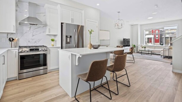 Una cocina moderna con armarios blancos, electrodomésticos de acero inoxidable y una isla central con taburetes de bar.