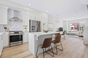A modern kitchen with white cabinetry, stainless steel appliances, and a central island with bar stools.