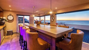 A modern bar area with a large island, bar stools, and a view of the ocean.