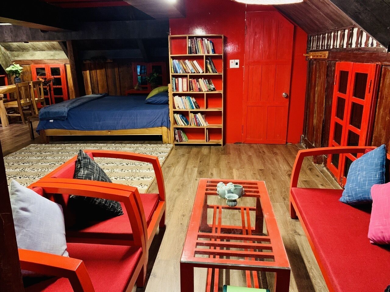 A cozy room with a bed, a bookshelf, and a dining area with chairs and a table.