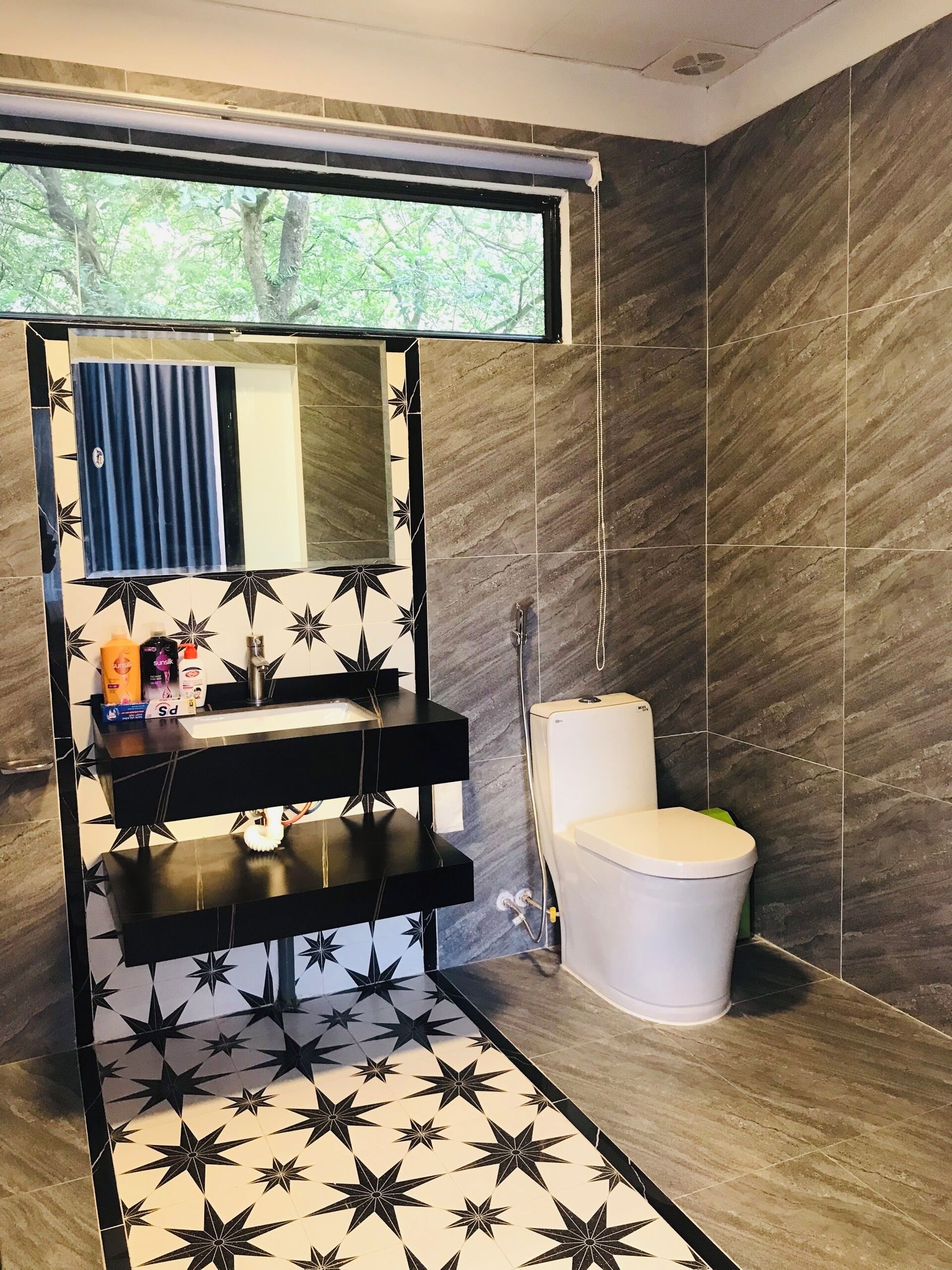 A bathroom with a black and white star-patterned floor, a white toilet, and a mirror above a black shelf with toiletries.