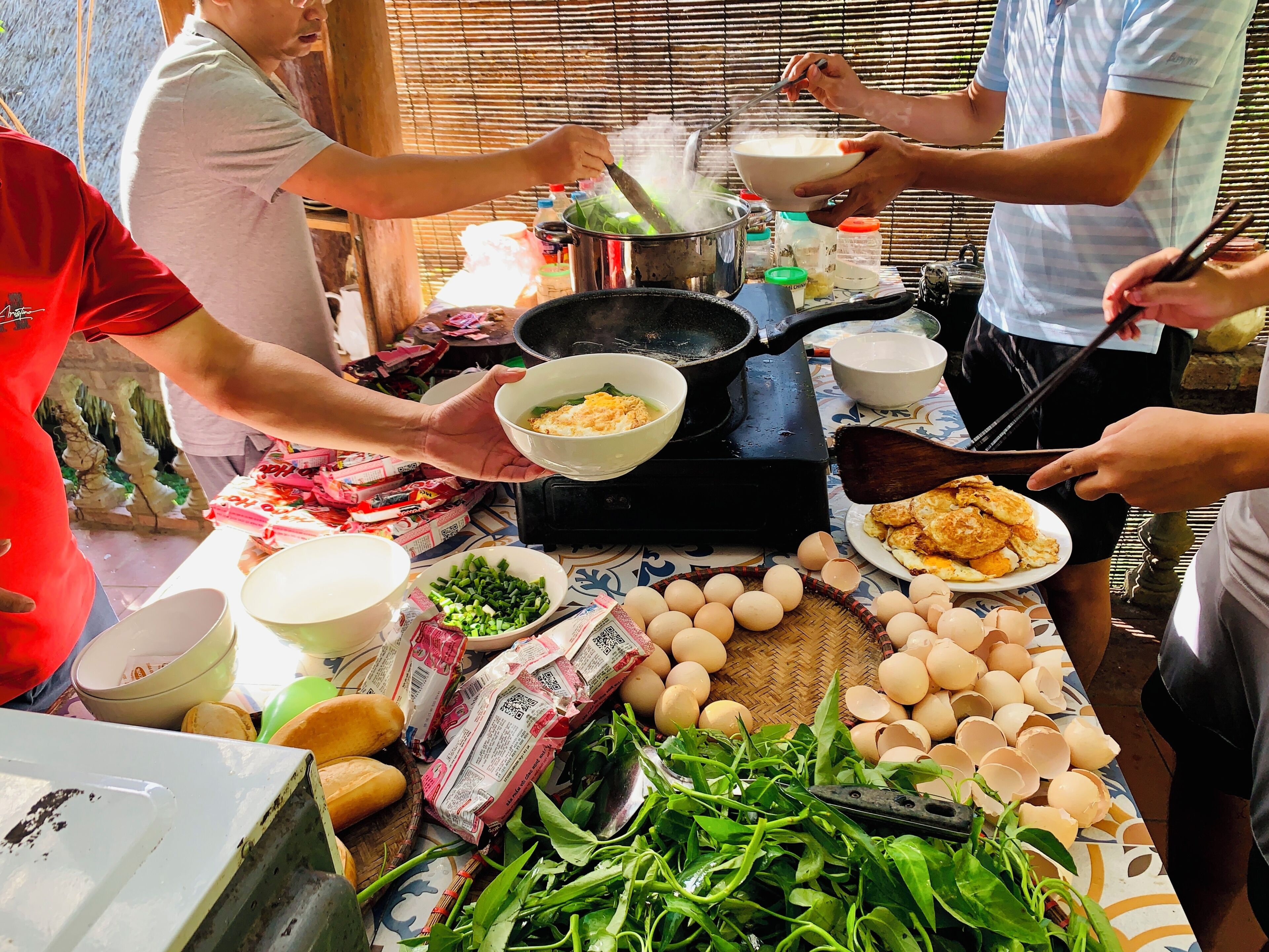 A group of people cooking outdoors with a table full of ingredients and cooking utensils.