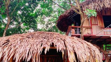 A rustic wooden structure with a thatched roof, surrounded by lush greenery.