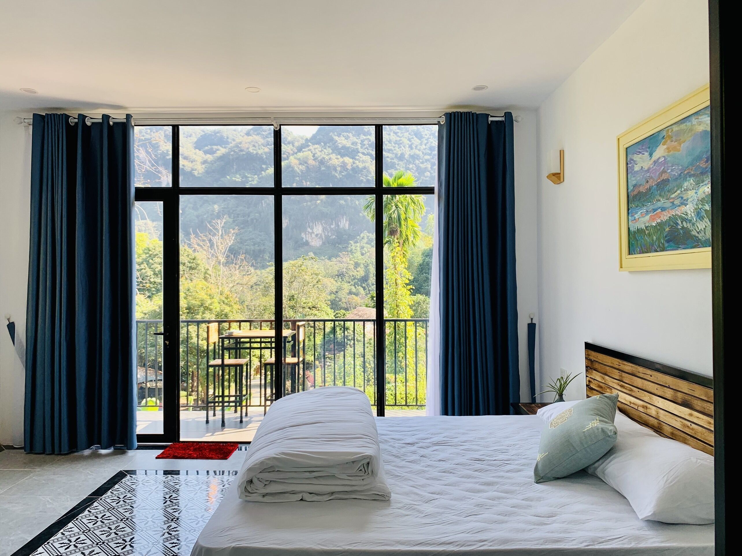 Habitación de hotel con un ventanal grande, cama con ropa blanca, cabecero de madera y un cuadro en la pared.