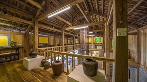 A rustic interior with wooden beams, a balcony with a railing, and several large vases displayed on pedestals. - Muong Retreat (Thong Nhat)
