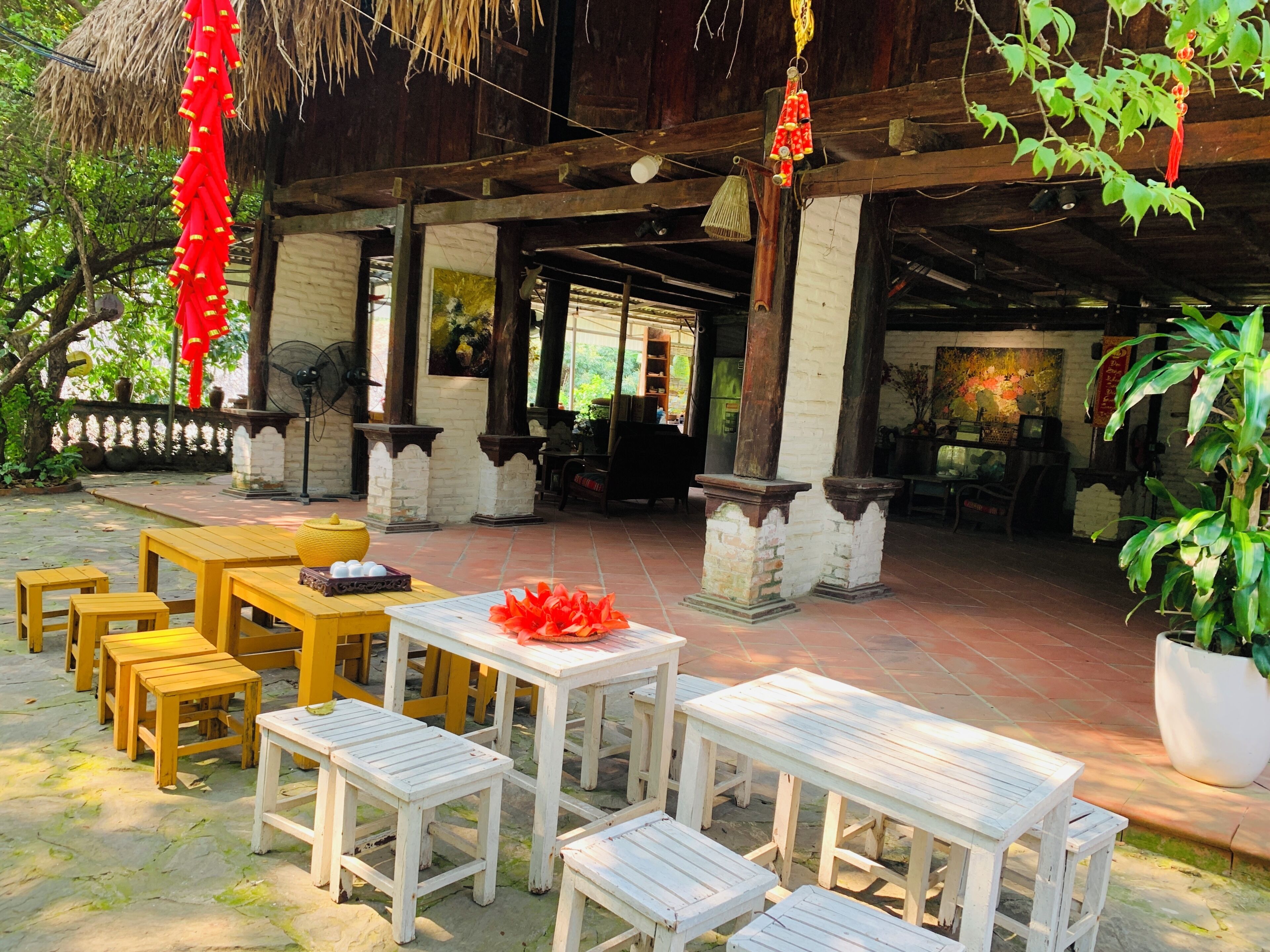 An outdoor seating area with wooden tables and chairs, a thatched roof, and potted plants.