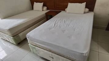 Una habitación con dos camas individuales, cabecero de madera, una mesita de noche pequeña y un armario de madera.