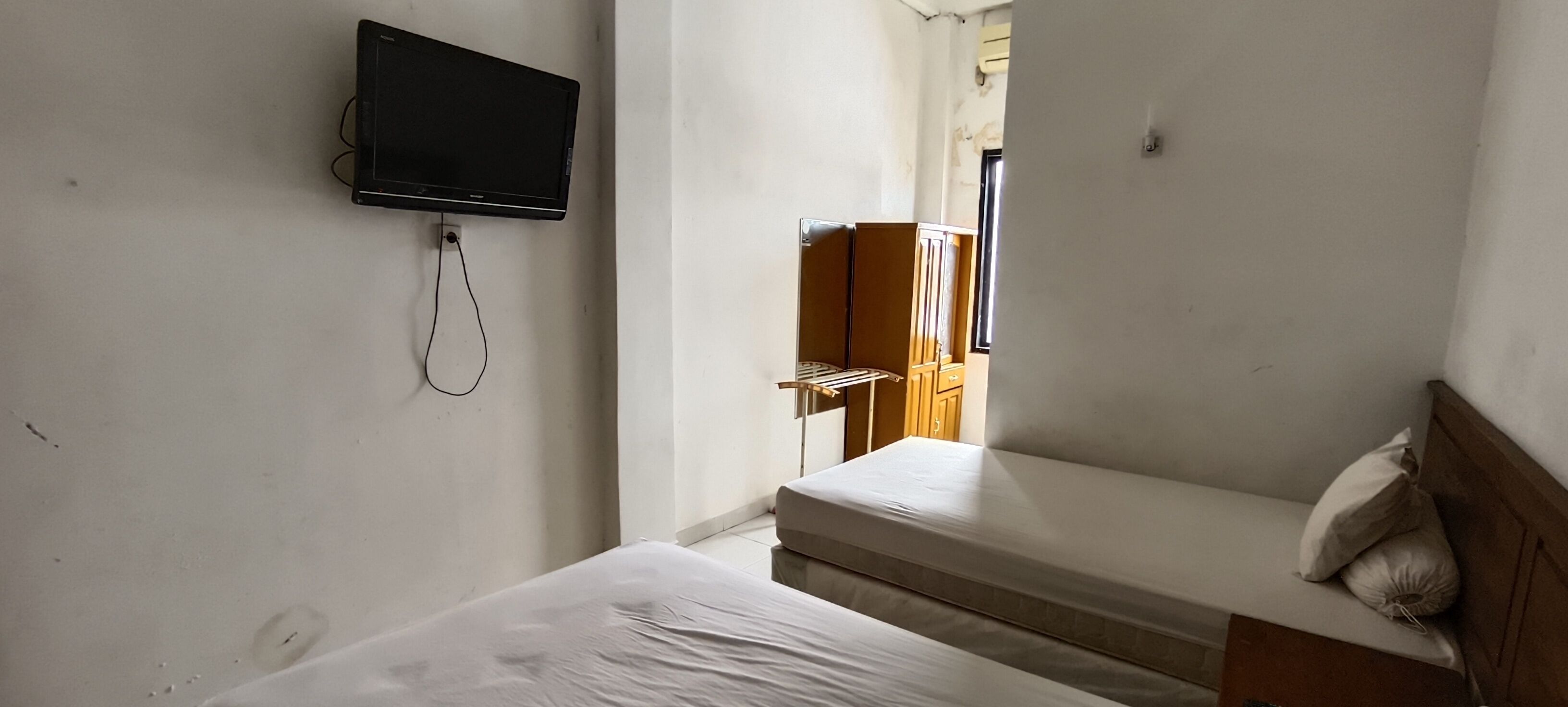 A small, narrow room with a single bed, a television mounted on the wall, and a wooden wardrobe.