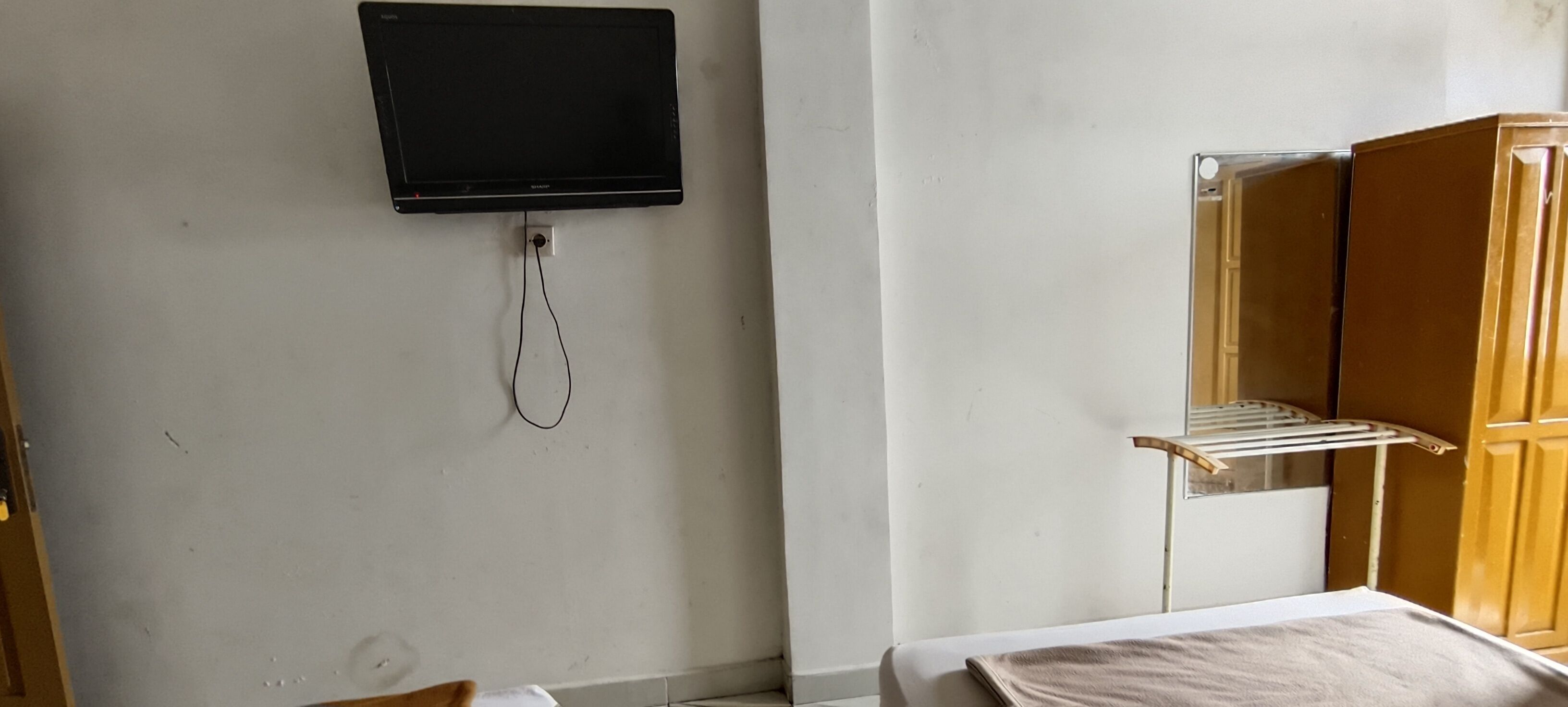 Habitació amb un llit, un televisor penjat a la paret i un estenedell.