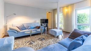 A modern living room with a light blue sofa, a glass coffee table, and a television on a stand. - Hafenriff - Appartement 1 (Sassnitz)