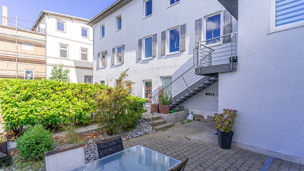 A residential building with a glass table and chairs in the courtyard, surrounded by greenery and a small staircase. - Hafenriff - Appartement 1 (Sassnitz)