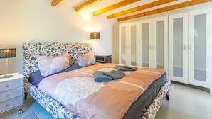 Quarto com uma cama, mesa de cabeceira, luminária, guarda-roupa e teto com vigas de madeira.