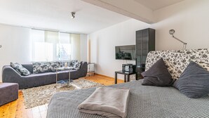 Uma sala de estar moderna com um sofá cinzento, uma poltrona estampada e uma janela grande.