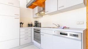 Uma cozinha compacta com armários brancos, forno embutido, lava-louças e cafeteira.
